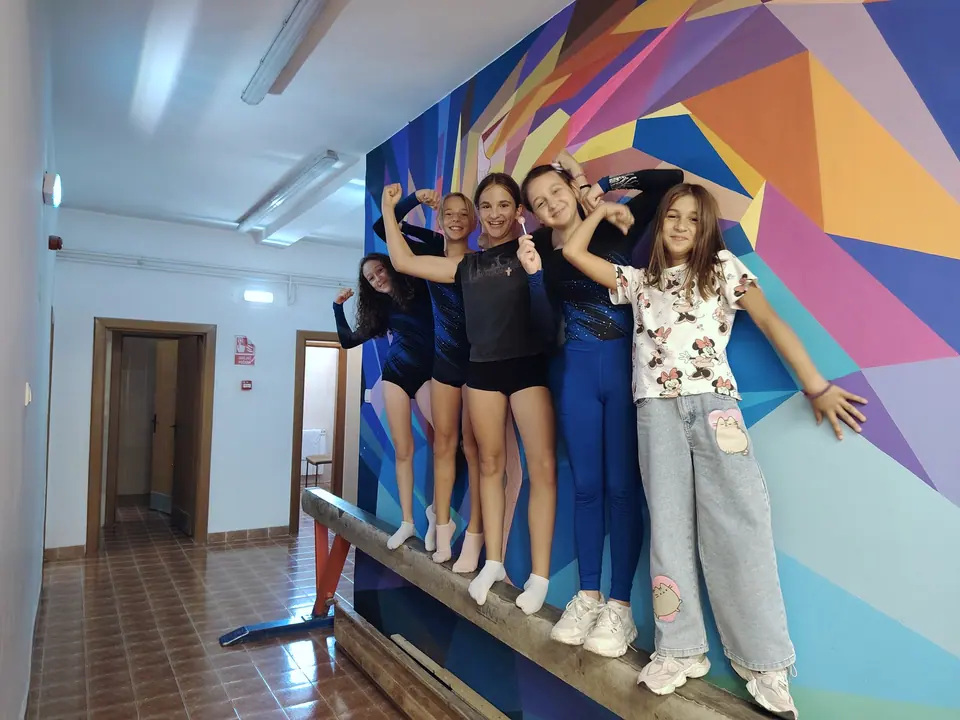 Gimnastičarke poziraju na gredi ispred šarenog geometrijskog murala